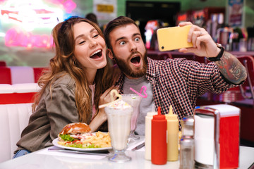 Poster - Young loving couple sit in retro bright cafe take a selfie