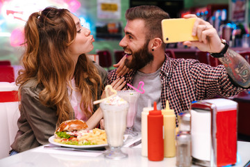 Poster - Young loving couple sit in retro bright cafe take a selfie