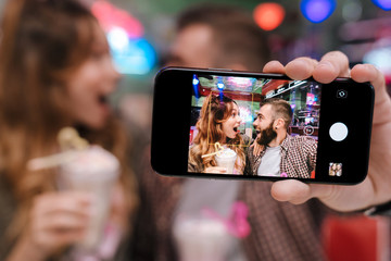 Poster - Young loving couple sit in retro bright cafe take a selfie