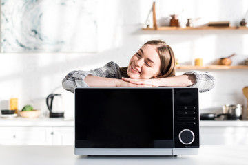 Wall Mural - smiling and attractive woman lying on microwave in kitchen