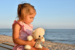 © sonsedskaya - Sad little girl with a toy bear sitting on the beach
