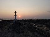 Fototapeta Krajobraz - The Christian cross on the rocks by the sea against the sunset.