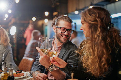Fotomural Cute caucasian couple sitting in restaurant and cheering with wine
