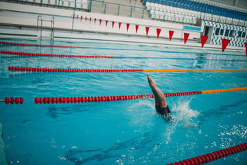 Young woman swimmer jumping in swimming pool. Legs over water.