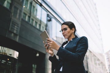 Serious spectacled businesswoman using tablet in downtown