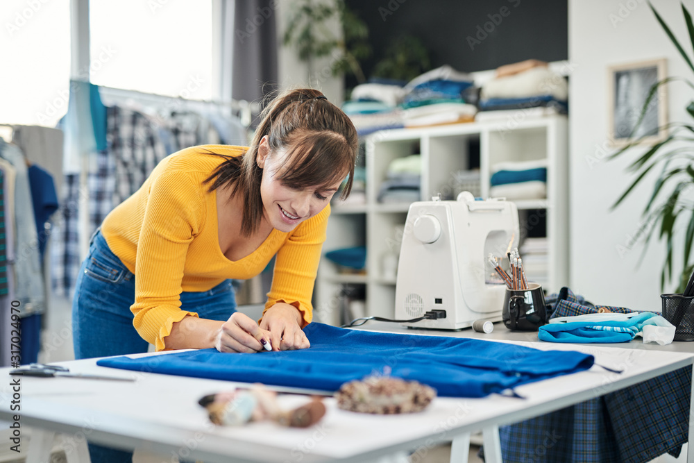 Charming caucasian smiling dedicated seamstress drawing  seam with chalk on a skirt. - obrazy, fototapety, plakaty 