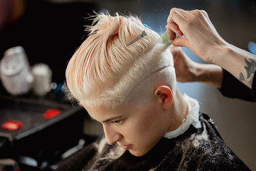 Hairdresser machine cuts woman client. A short haircut, shaved temple and a drawing on the hair.