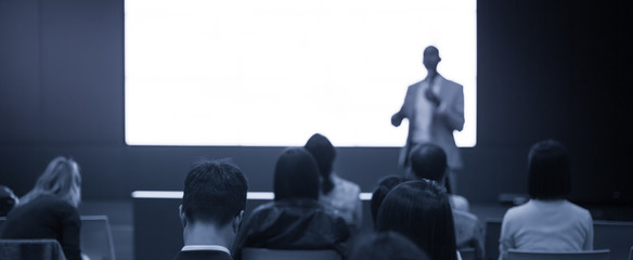Fototapete - Speaker on the stage with rear view of audience in the conference hall or seminar meeting, business and education concept. Speaker giving a talk at business meeting. Seminar presentation photo.