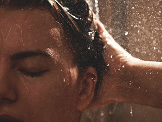 Girl in the shower under stream of water washes her hair, wet face close-up, enjoys eyes closed