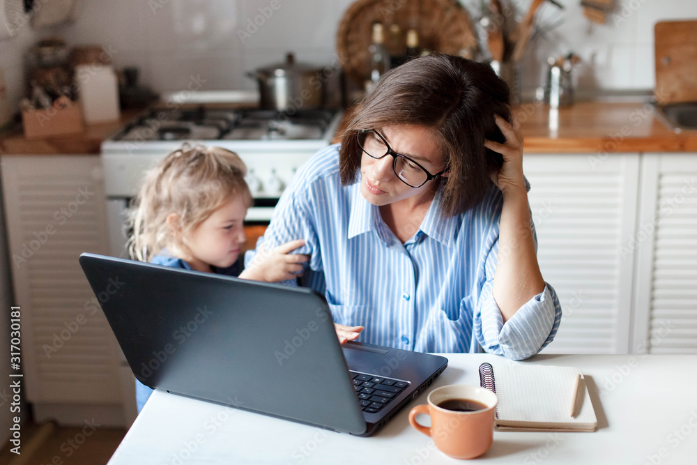 Working mother in home office. Unhappy woman and child using laptop. Sad and angry daughter needs attention from busy exhausted mom. Freelancer workplace in kitchen. Female business. Lifestyle moment. - obrazy, fototapety, plakaty 