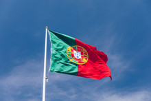 Beautiful Large Portuguese Flag Waving In The Wind Against Blue Sky. Portuguese Flag Waving Against Blue Sky. Flag Of Portugal Waving, Against Blue Sky