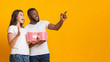 © Prostock-studio - Excited interracial couple holding popcorn backets and pointing at copy space