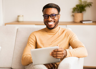 Poster - Man In Eyeglasses Holding Tablet Sitting On Couch At Home