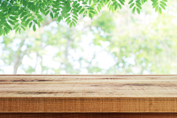 Wall Mural - Wooden table and blurred green leaves nature background.