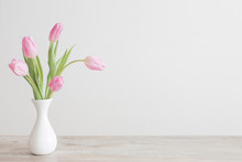 Pink Tulips In White Ceramic Vase On Wooden Table On Background White Wall