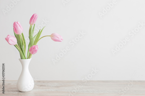 Fotografía pink tulips in white ceramic vase on wooden table on background white wall