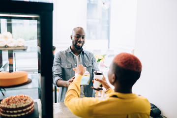 Wall Mural - Positive black guy buying coffee and cake in bakery