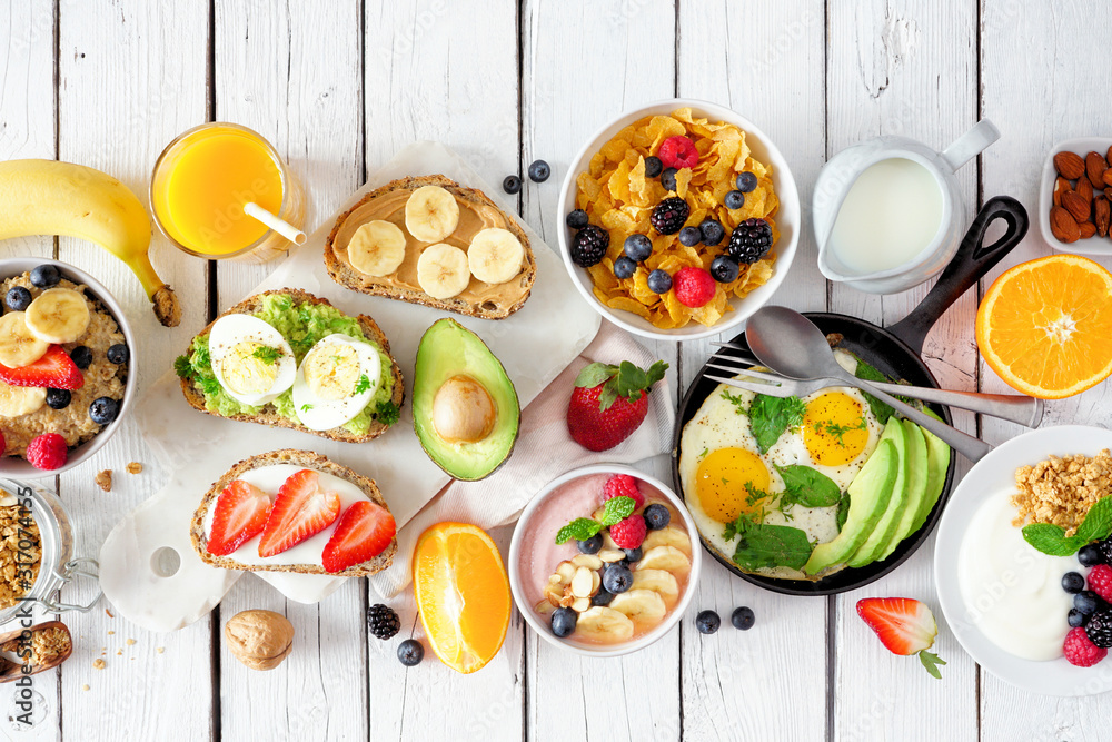 Healthy breakfast table scene with fruits, yogurts, oatmeal, cereal, smoothie bowl, nutritious toasts and egg skillet. Top view over a white wood background. - obrazy, fototapety, plakaty 