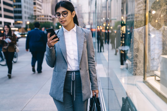 Confident young formal pretty business lady surfing smartphone on street