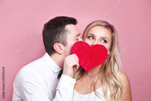 Photographie Young couple holding red love heart over eyes and kissing