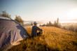 © Svetlana - Hiker in hat sits near tent meets good morning on top of mountains