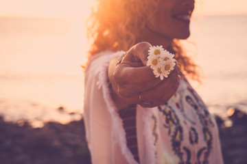 Sticker - Environment and love for nature concept with cheerful happy woman in background holding some beautiful daisies with the hand - sun in backlight - sunset time