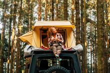 Travel And Wanderlust Lifestyle Concept With Happy Lonely Adult Woman Sit Down On The Roof Tent Car Vehicle With Wood Forest In Background Enjoying Nature And Outdoors Vacation