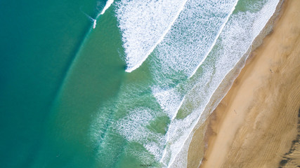 Australian beach with two people walking really close to the water. In the image we can see a colorful beach with some waves on it.