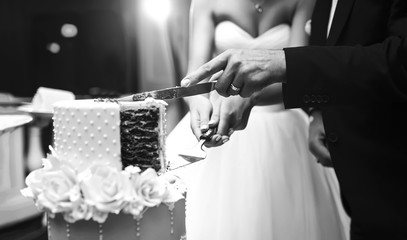 Wall Mural - Black and white photo of couple hands cutting wedding cake. Happy bride and a groom is cutting their beautiful wedding cake on wedding banquet. Wedding and celebration concept.