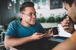 © BullRun - Excited young male businessman sharing good news with colleague on smartphone in cafe
