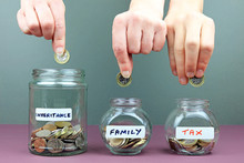 Hands Putting In To Different Money Jars. Spreading Your Inheritance Money Around Concept.