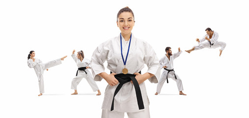 Young female karate champion with a medal posing with people practicing behind