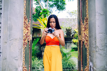 Focused young Asian woman photographing with camera in street