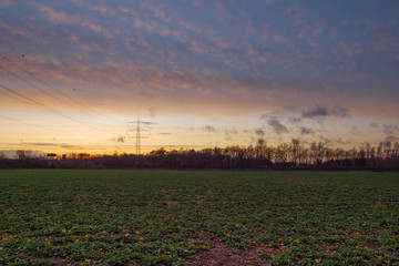 Beautiful dramatic orange, gold and blue cloud and sky after storm and rain over agricultural field and high voltage tower on countryside in Germany. Nimbostratus cloud during sunset. 