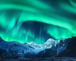 Wall Mural - Aurora borealis above the snow covered mountain peak in Norway. Northern lights in winter. Night landscape with green polar lights and snowy mountains. Starry sky with aurora over the rocks. Space