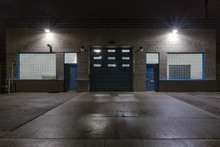 Two Blue Doors And A Large Garage Door On The Back Of An Industrial Building At Night With Star Burst Lights