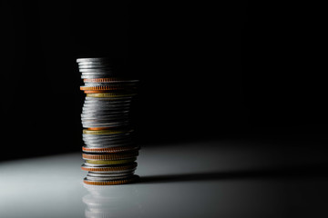 a tall stack of coins, mostly silver with a few gold and copper ones, on a white surface. The background is dark.