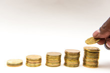 Canadian Dollar Coins Tacked Into Five Ascending Piles On White Background. Hand Can Be Seen Taking Or Adding A Coin To The Pile.