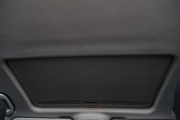 View of the ceiling of the car with a transparent glass hatch for airing, opening so that you can see the sky and clouds in the gray cabin of the vehicle. Sunroof on beige roof.