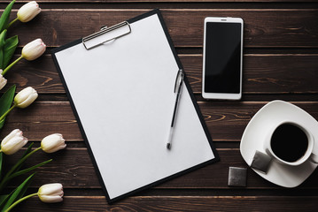 Wall Mural - White tulips on a wooden table with an empty paper tablet and smartphone and a Cup of coffee