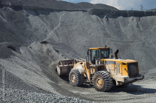 Fotomural Wheel loader excavator fills the bucket with rubble in the warehouse of products in the open air