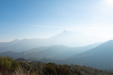 Wall Mural - Sun flare shining on a solid blue sky on a foggy mountain landscape