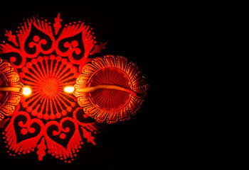 Top shot of two glowing terracotta lamps and rangoli against dark background. festival of light concept