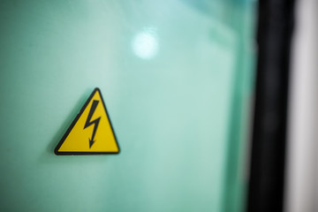 Sign danger high voltage. Sign dangerously high voltage electricity. A yellow triangle mark with a lightning bolt in the center. This warning is painted on an old metal surface painted with gray paint