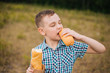 © Вероника Преображенс - The boy eats a long loaf of bread. Picnic in nature. The guy in the blue plaid shirt