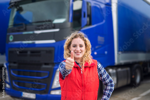 Portrait of professional truck driver showing thumbs up and smiling. Truck vehicle in background. Transportation services. Trucker occupation.