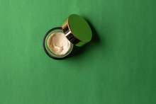Cosmetic Cream With Olive Oil In A Green Glass Jar With A Gold Cap On A Green Background