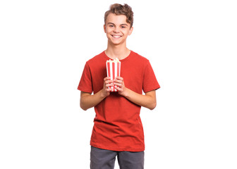 Poster - Portrait of smiling teen boy with popcorn bucket, isolated white background. Happy child preparing to watch the film while holding popcorn. Handsome funny teenager looking at camera.