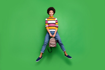 Poster - Full length photo of cheerful funky careless afro american girl hold stylish backpack jump enjoy autumn holiday wear denim jeans isolated over green color background