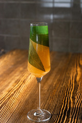 A gold cocktail served in a champagne glass on the wooden bar table and decorated with green bamboo leaf inside